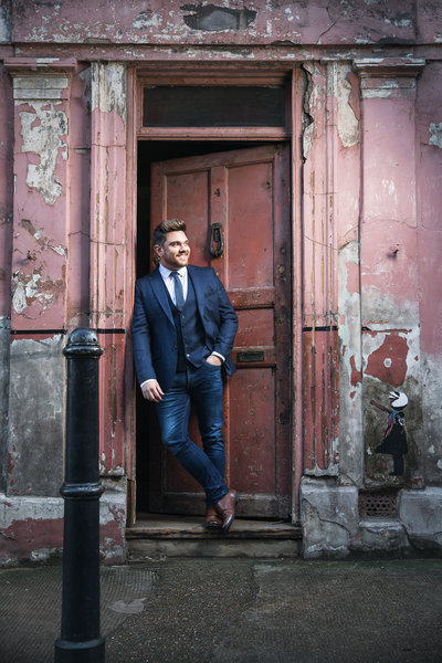 Mark Kingswood singer posing by a door wearing a suit.